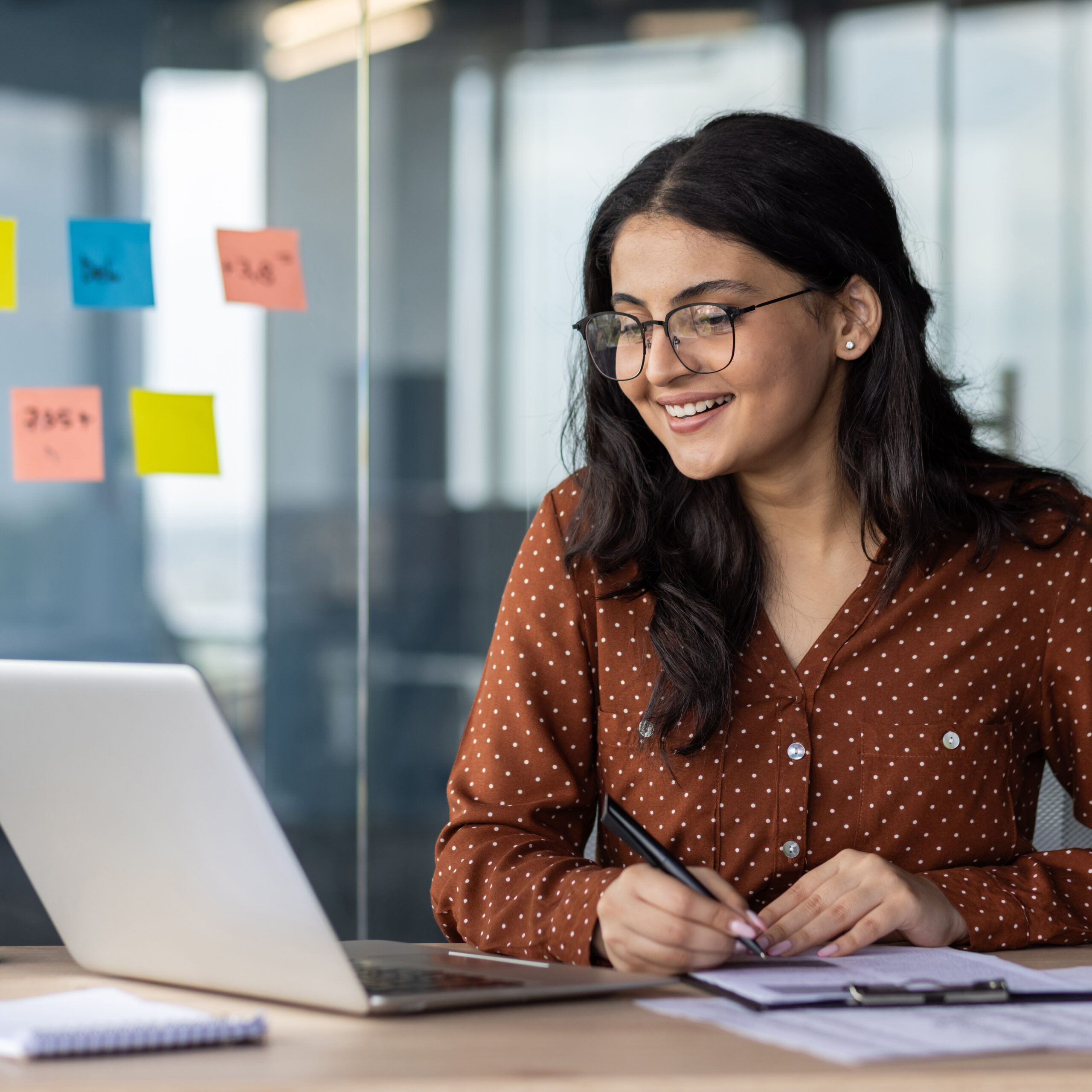 happy-woman-financier-doing-paperwork-inside-office-latin-american-smiling-pleased-preparing-financial-report-accountant-recording-data-and-filling-forms-sitting-at-table-with-documents-and-laptop