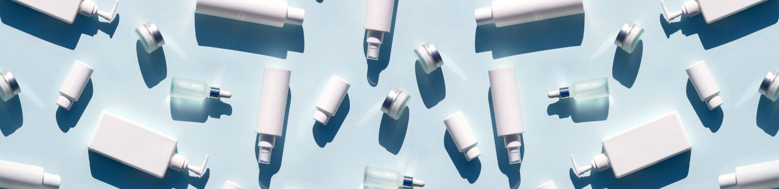 Banner made with white bottles and jars of cosmetic products and strong shadow on blue background, as backdrop or texture. Creative layout for your design