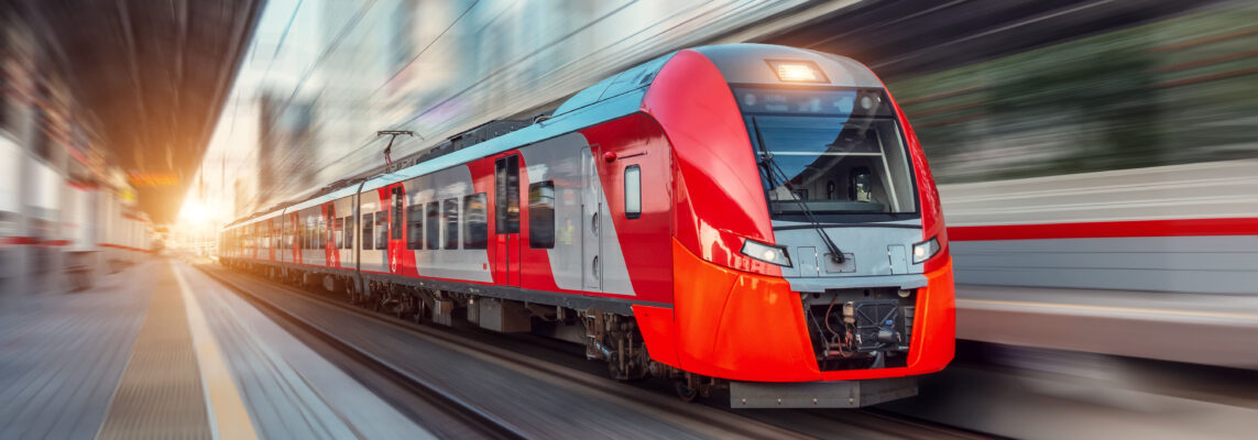 Electric passenger train drives at high speed among urban landscape.